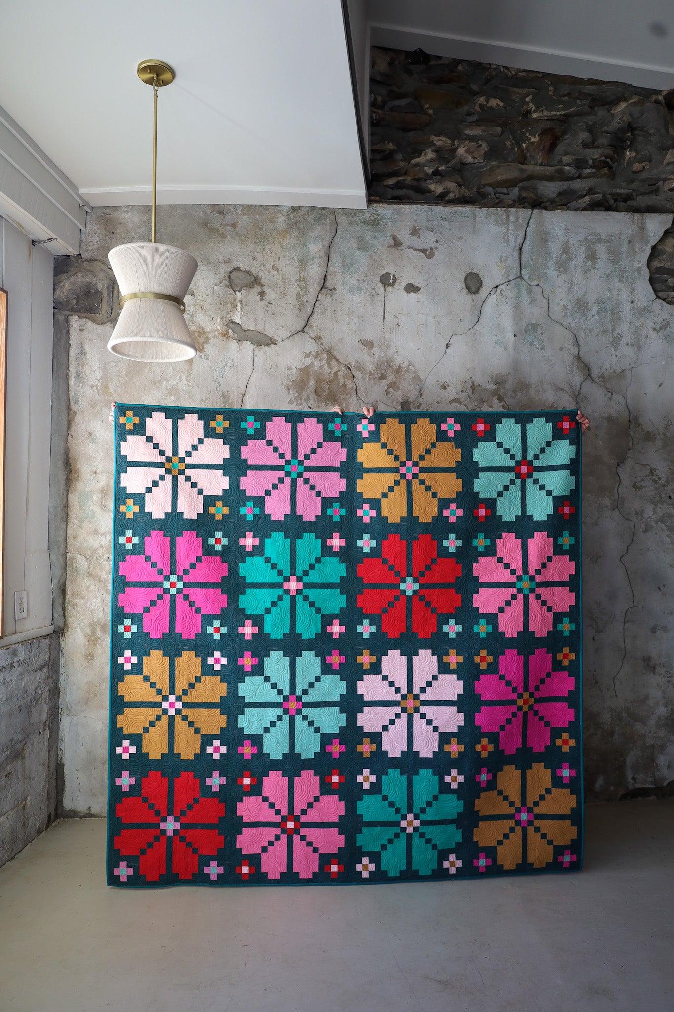 Knitted Blooms Holiday sample quilt held up against a textured wall