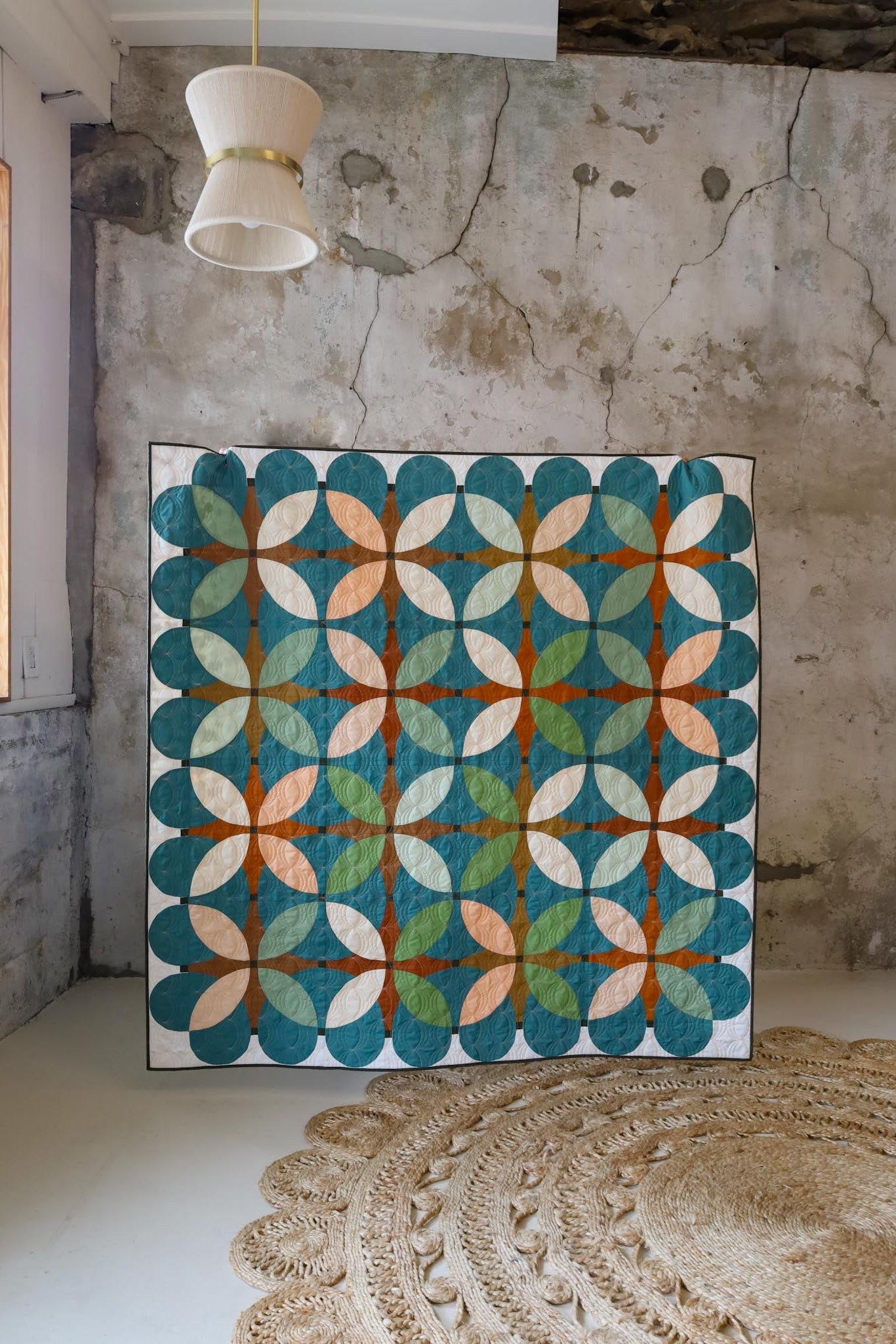 Retro Blossoms Hemlock sample quilt held up in a room with a rug and textured wall