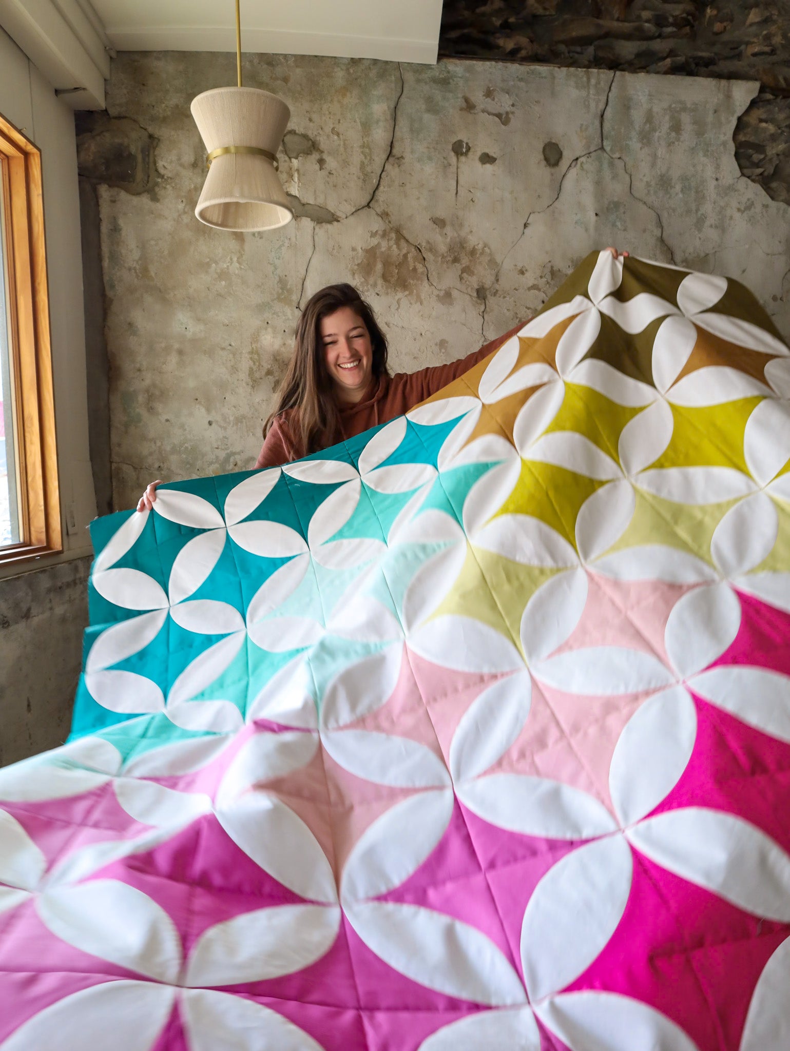 Brittany holding the sample cover quilt. Shades of Citrus 2.0 quilt paper pattern by Lo & Behold Stitchery featuring an orange peel ombre design comes in 7 sizes. 