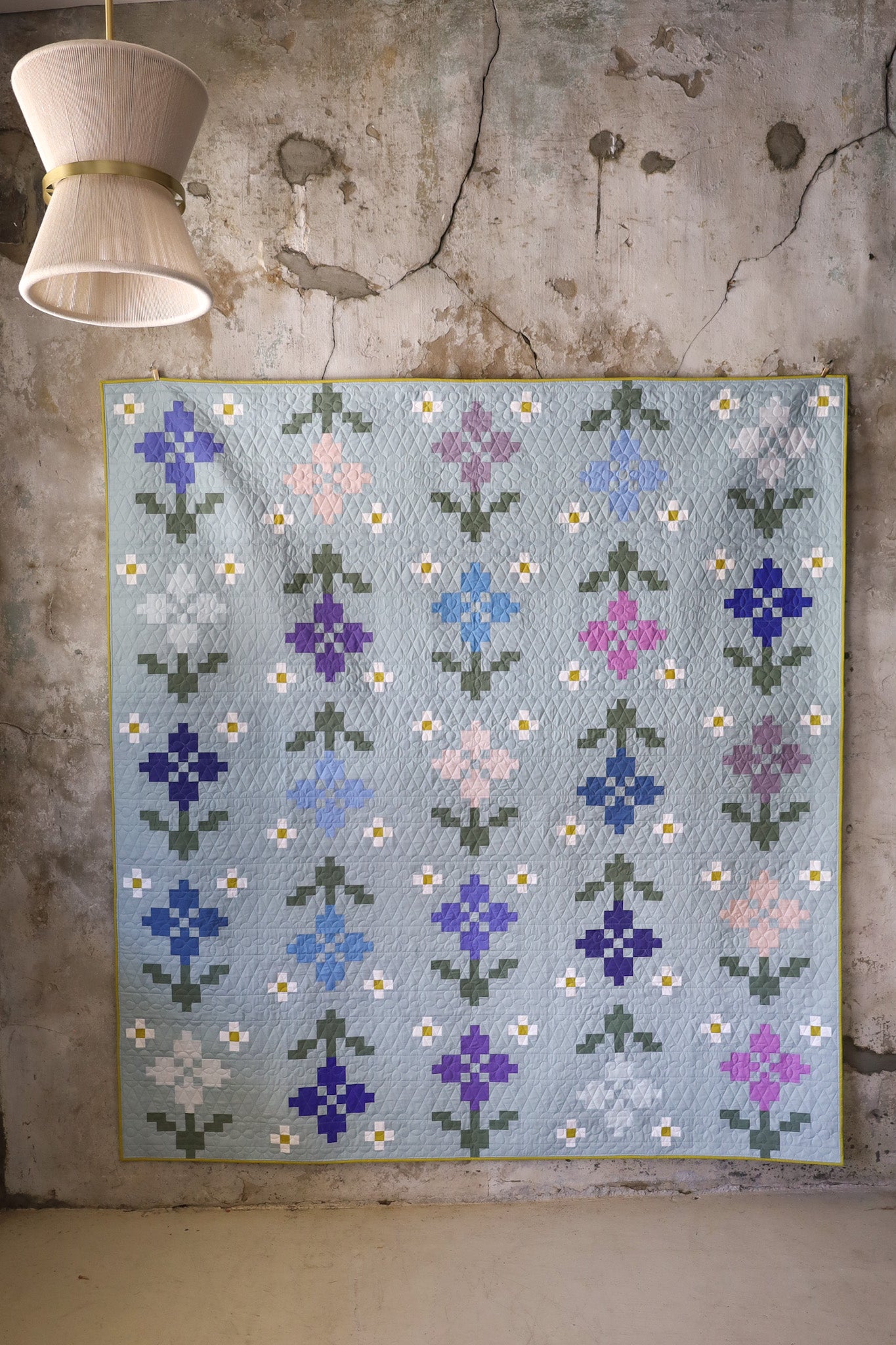 Pansy Patch Forget-me-not quilt sample hanging on textured wall