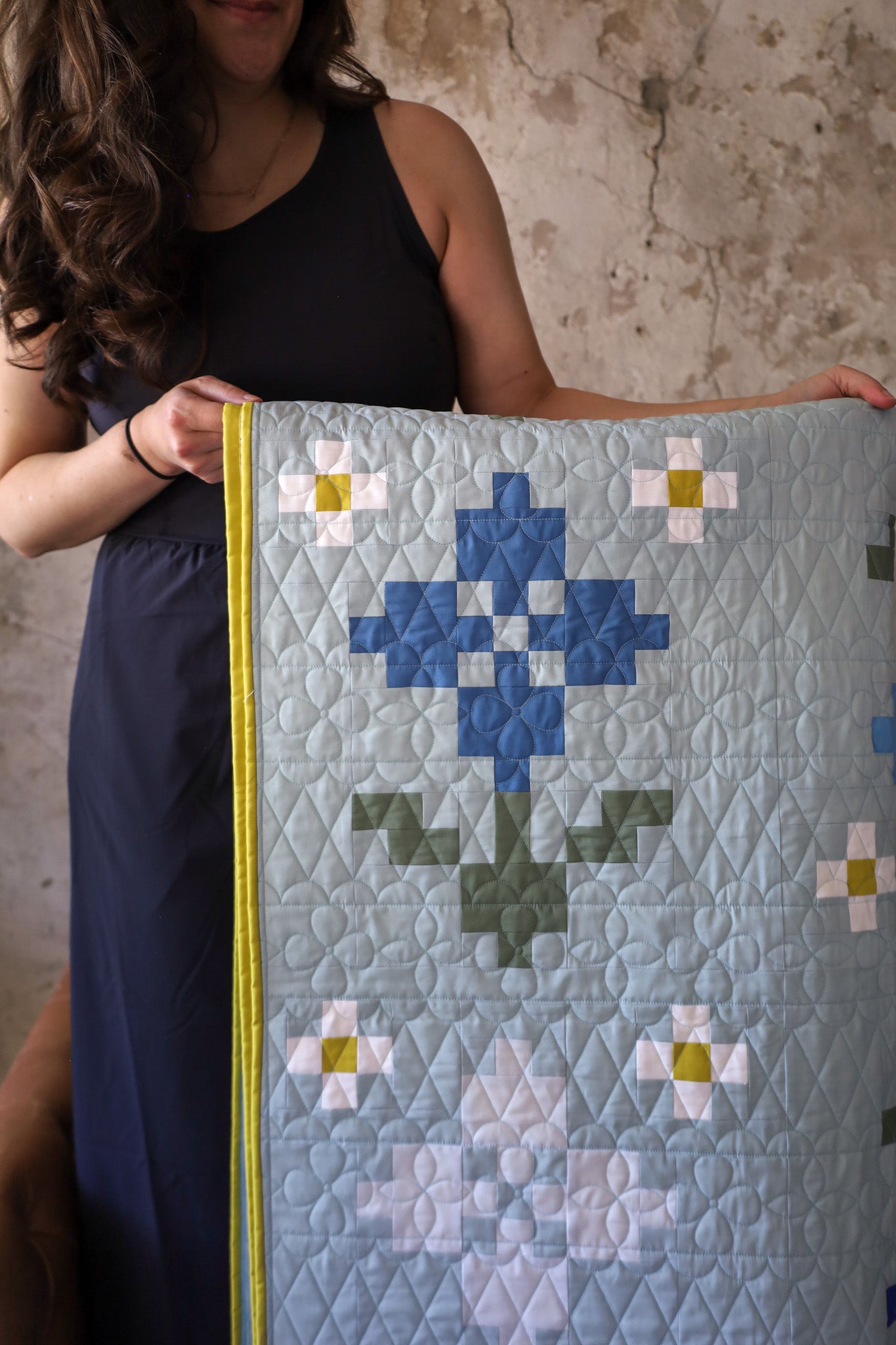 Brittany holding a pansy patch sample quilt. A quilt pattern by Lo & Behold Stitchery. Nine sizes, 3 colorways, fat quarter friendly.