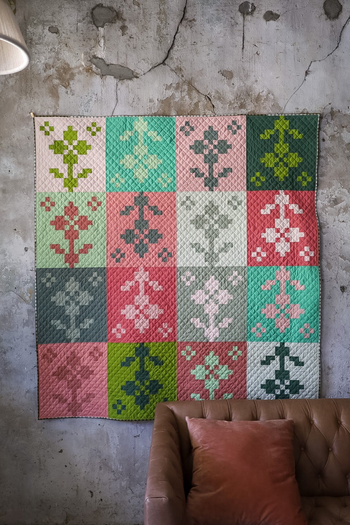 Pansy Patch Sprout quilt sample hanging on textured wall behind brown couch and pink pillow